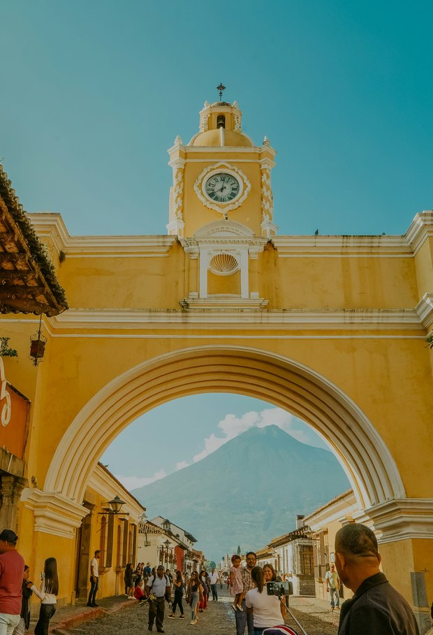 The yellow Santa Catalina arch with its clock tower, framing the cone of Volcán de Agua down the cobbled street.