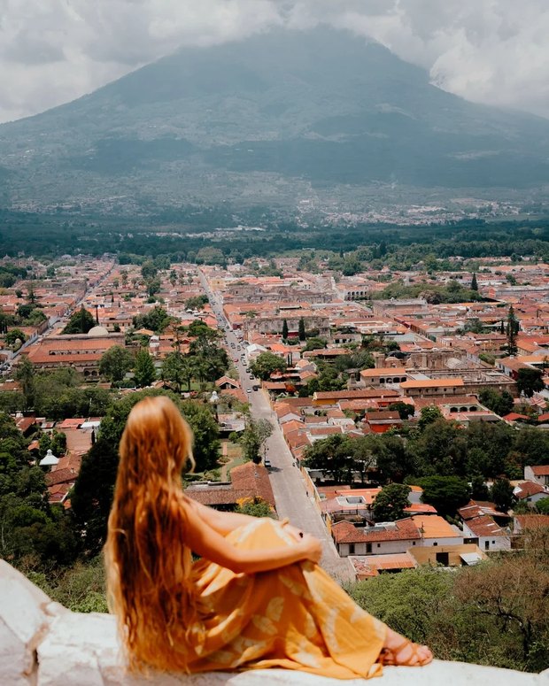 The view from Cerro de la Cruz: the grid of orange rooftops and ruined churches running down to Volcán de Agua under cloud.
