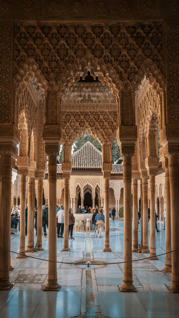 The Court of the Lions through a screen of slender columns and carved plaster arches, the lion fountain in the middle of the courtyard.