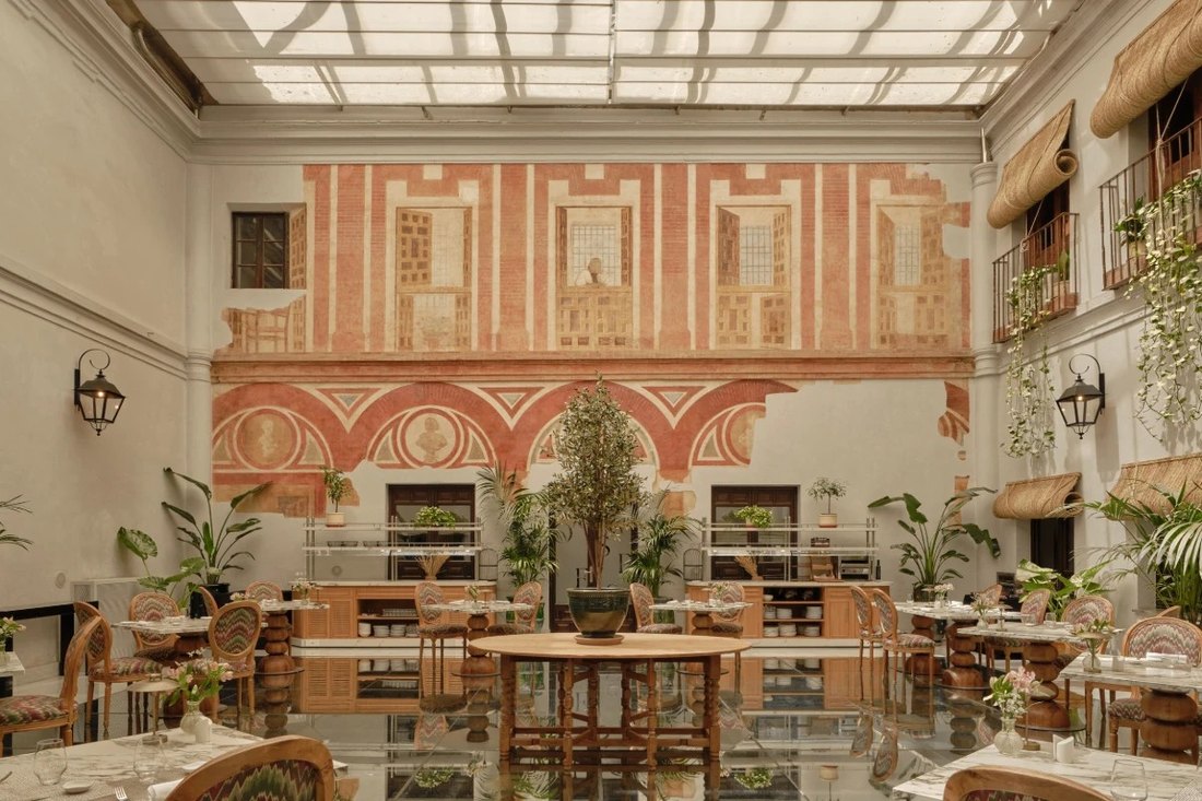 The covered courtyard dining room: faded red-and-cream Renaissance frescoes on the walls, balconies with trailing plants, and tables set on a glass floor.