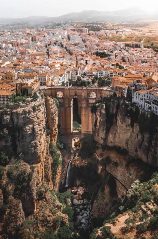 Ronda from the air: the stone Puente Nuevo spanning the deep gorge, a waterfall below and the white town spreading back behind it.