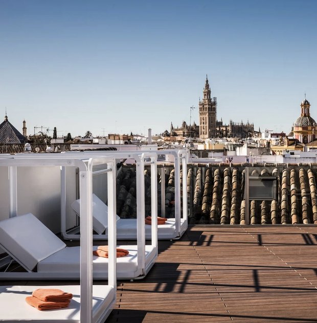 The roof terrace: white daybeds on a wooden deck, with the Giralda over the old-town rooftops.